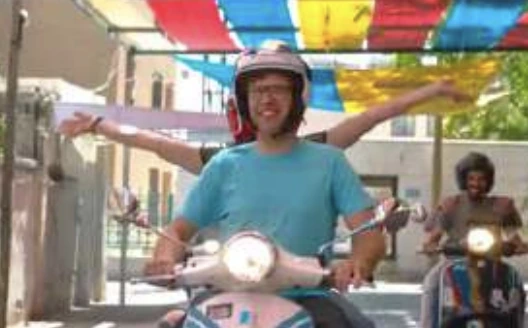 Robert Abboud riding a scooter in a street scene
